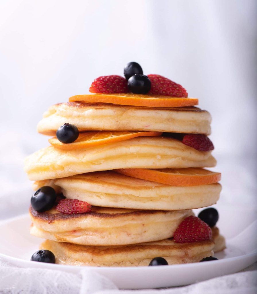 Stapel pannenkoeken met sinaasappelschijfjes en rood fruit